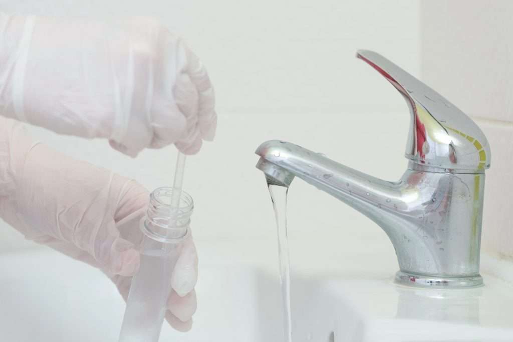 A gloved hand filling a test tub of water from a bathroom water fixture