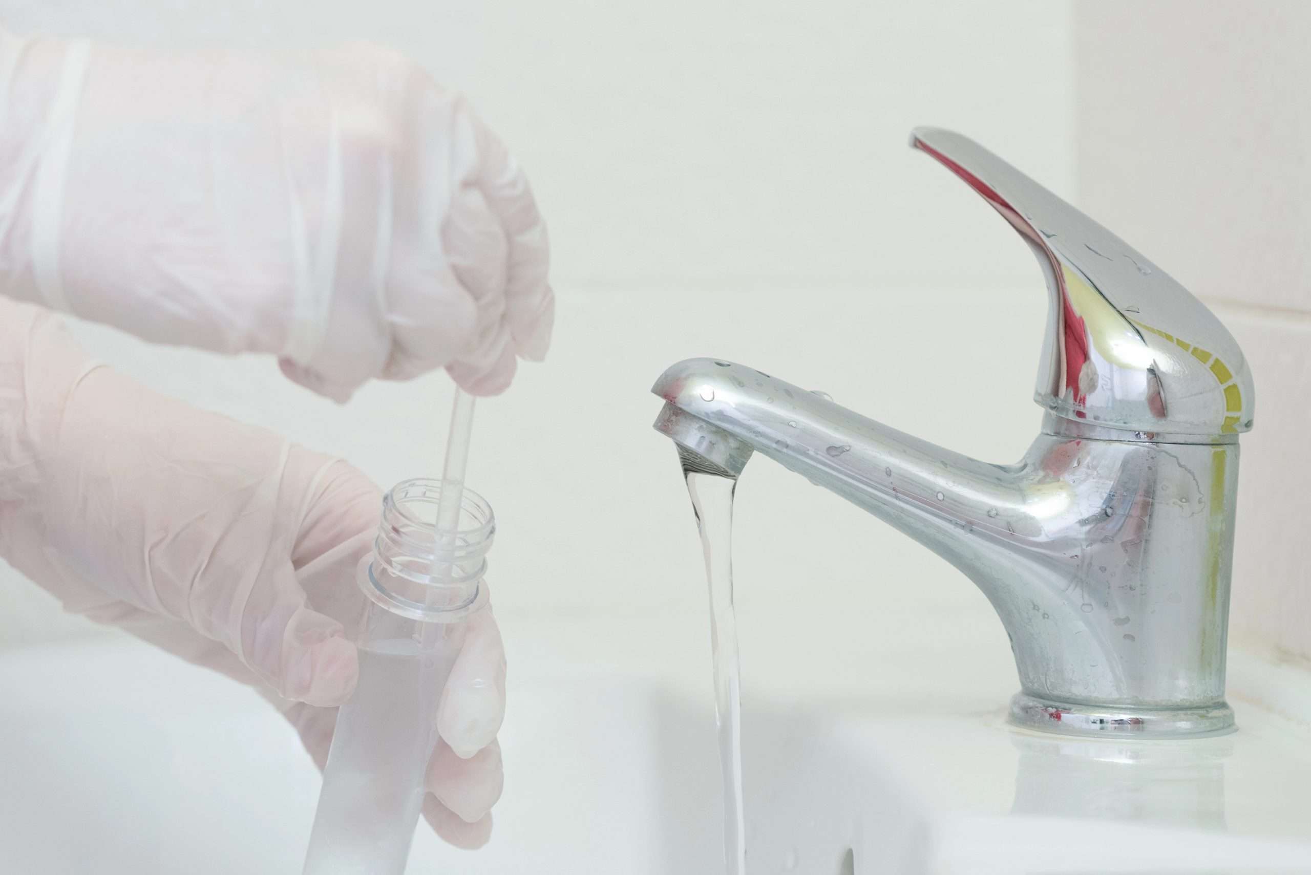 A gloved hand filling a test tub of water from a bathroom water fixture